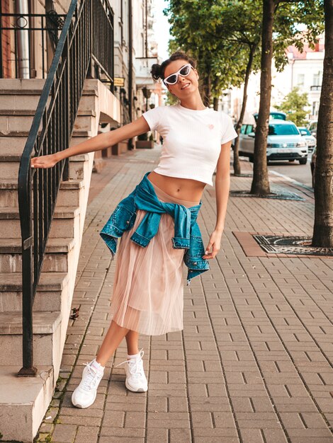 Beautiful smiling model with horns hairstyle dressed in summer hipster jacket jeans clothes.Sexy carefree girl posing in the street.Trendy funny and positive woman having fun in sunglasses