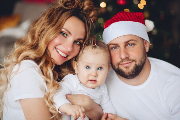 아름 다운 미소 어머니와 그들의 딸을 껴 안은 산타 모자에 아버지. 크리스마스 때.