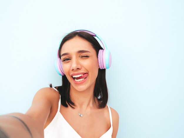 Beautiful smiling woman dressed in white pajamas. carefree model listening music in wireless headphones