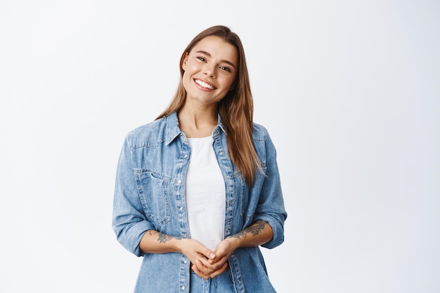 Beautiful smiling woman looking friendly and ready to help customer or client holding hands together and staring at camera white background