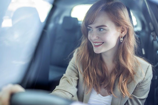 Foto gratuita bella sorridente giovane donna rossa dietro il volante che guida l'auto