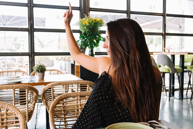 Beautiful smiling young woman raising her hand while calling for a waiter