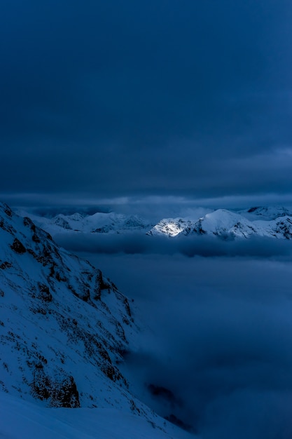 Красивые снежные холмы и горы ночью с захватывающим облачным небом