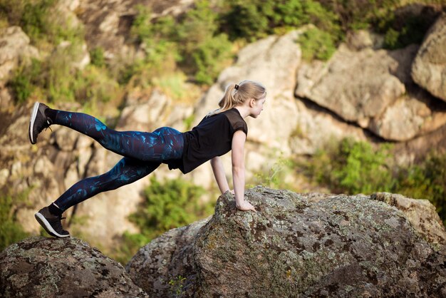 Beautiful sportive blonde woman stretching on rock in canyon