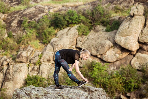 Beautiful sportive blonde woman training, stretching on rock in canyon