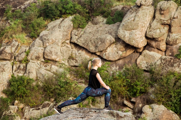 Beautiful sportive blonde woman training, stretching on rock in canyon