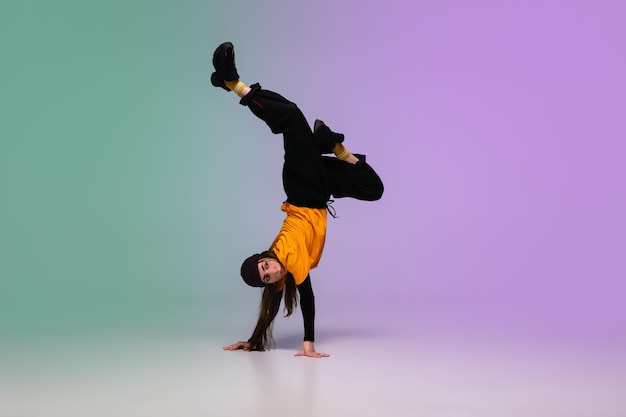 Beautiful sportive girl dancing hip-hop in stylish clothes on colorful gradient background at dance hall in neon light. Youth culture, movement, style and fashion, action. Fashionable bright portrait.