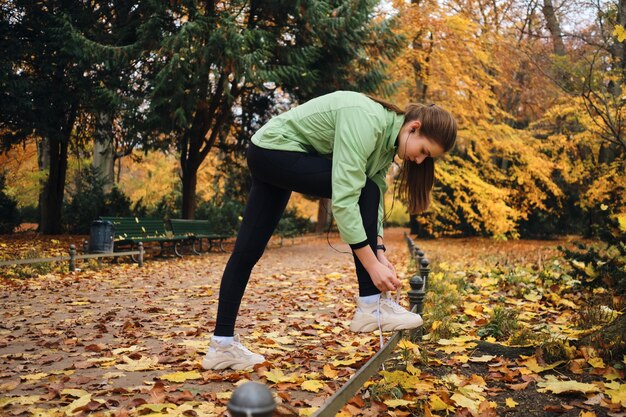 아늑한 가을 공원에서 달리기 전에 운동화에 신발끈을 묶는 아름다운 스포티 소녀