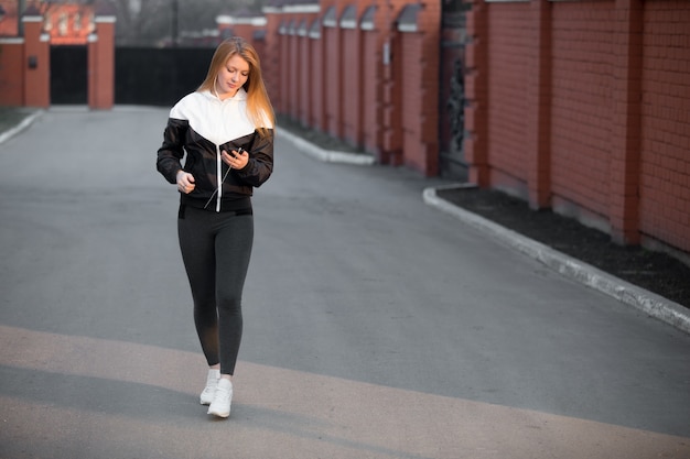 Beautiful sporty girl using device walking in the street