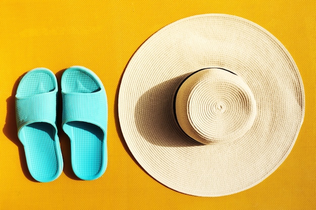 Beautiful straw hat with blue flip flops on yellow vibrant vivid background. Top View. Flat Lay. Summer Travel Vacation Concept. 