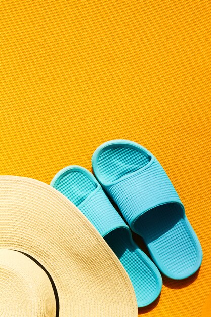 Beautiful straw hat with blue flip flops on yellow vibrant vivid background. Top View. Flat Lay. Summer Travel Vacation Concept. 