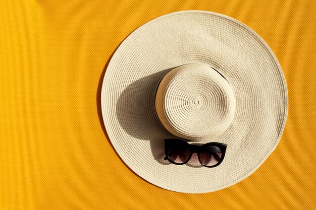Beautiful straw hat with sunglasses on yellow vibrant vivid background. Top View. Summer Travel Vacation Concept.