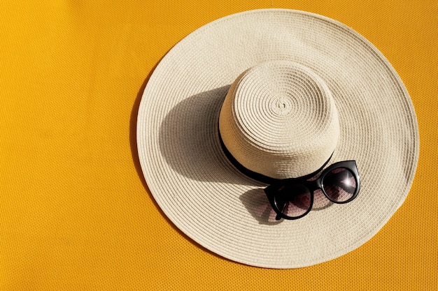 Beautiful straw hat with sunglasses on yellow vibrant vivid background. Top View. Summer Travel Vacation Concept.