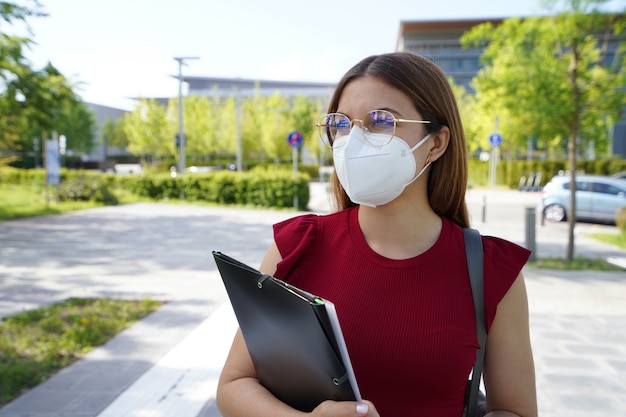 Beautiful student girl wearing ffp2 protective mask walking in modern street