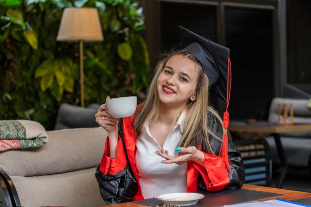 美しい学生はレストランで卒業ケープを着てコーヒーを飲みます