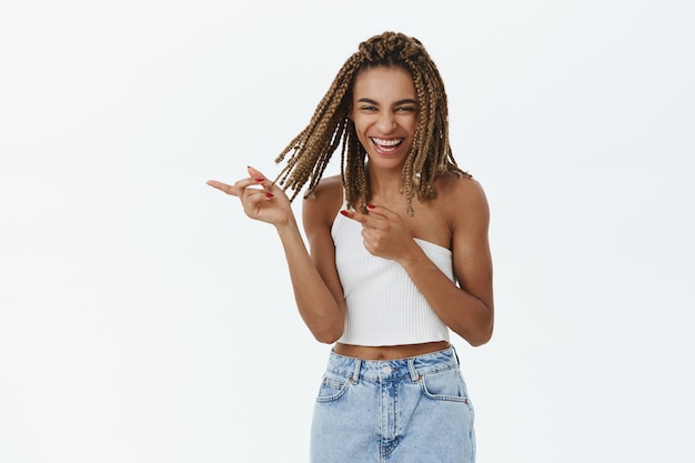 Beautiful stylish african-american girl smiling, pointing finger left at logo