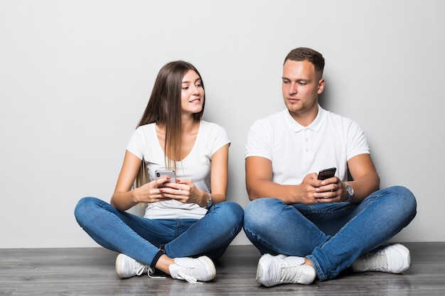 Beautiful stylish couple using their mobile phones together isolated on white background