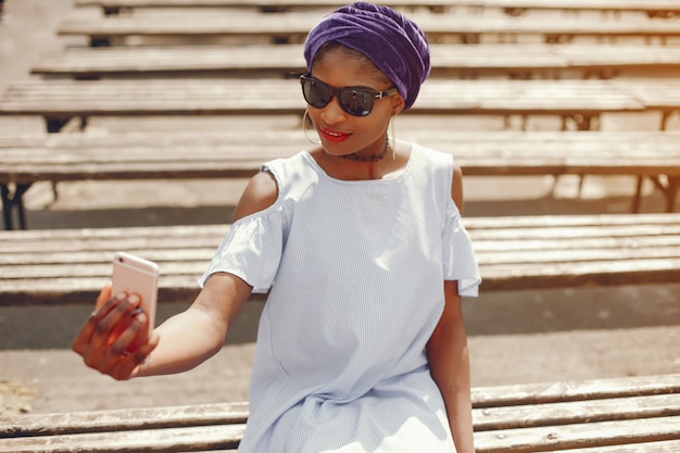 A beautiful and stylish dark-skinned girl walks in a sunny summer city