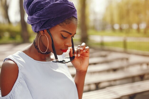 A beautiful and stylish dark-skinned girl walks in a sunny summer city