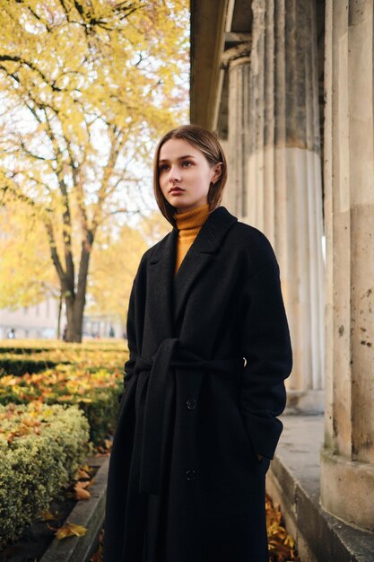 Beautiful stylish girl in black coat intently looking away on beautiful city street