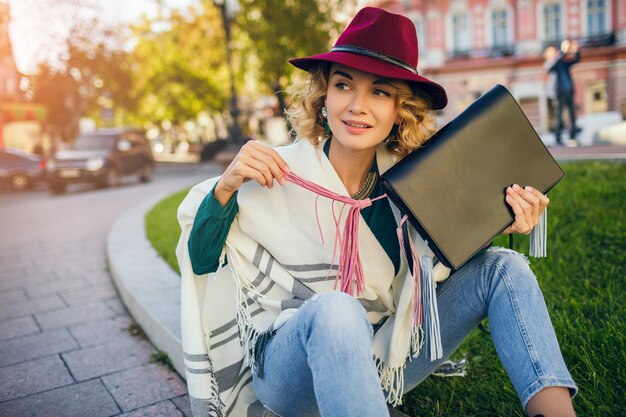 Beautiful stylish lady walking in street in cape holding handbag, fashion accessories, spring street style trend, smiling