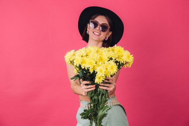 Beautiful stylish woman in hat and sunglasses posing, holding large bouquet of yellow asters, spring mood, positive emotions isolated