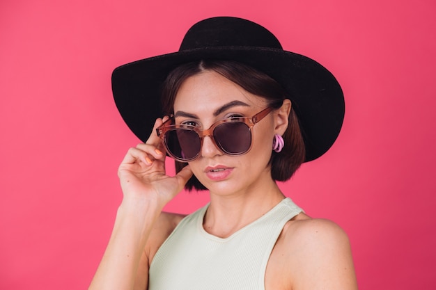 Beautiful stylish woman in hat and sunglasses posing over pink red wall
