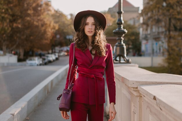 Free photo beautiful stylish woman in purple suit walking in city street, spring summer autumn season fashion trend wearing hat, holding purse