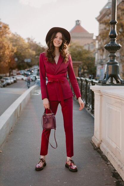 Красивая стильная женщина в фиолетовом костюме гуляет по городской улице, модная тенденция сезона весна-лето-осень в шляпе, держа кошелек