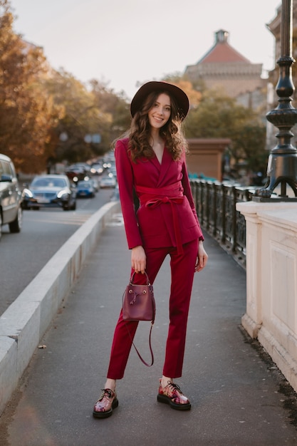 Foto gratuita bella donna alla moda in vestito viola che cammina nella via della città, tendenza di moda primavera estate autunno stagione indossando il cappello, tenendo la borsa