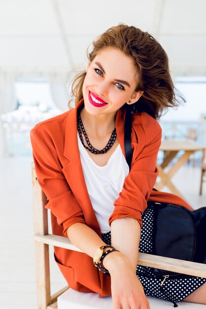 Beautiful stylish young friendship girl  sitting in summer restaurant  and  dreaming.  Happy sunny summer vacation mood, bright colors. Have full red lips and big blue eyes.