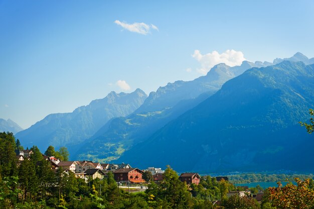 山の近くに小さな家がある美しい夏の風景。スイスアルプスの大きな緑の山の牧草地のある風景