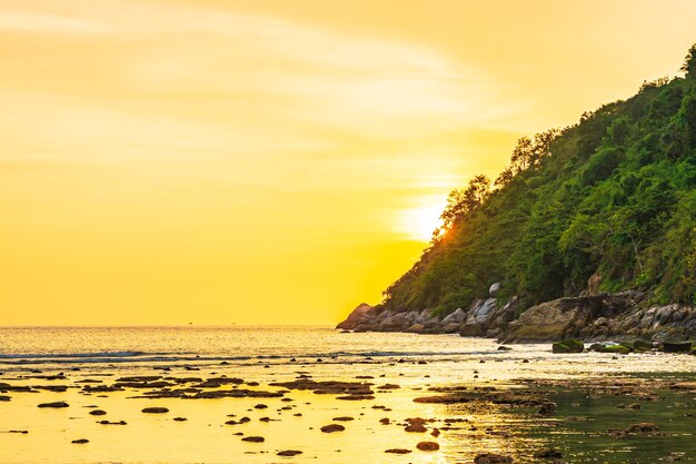 ビーチ、海、海、岩の周りの山に沈む美しい夕日