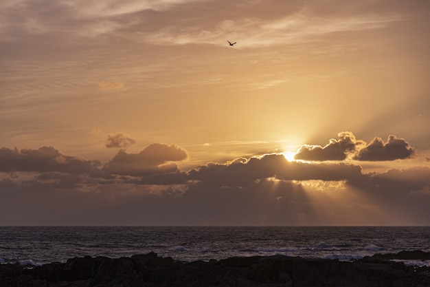 大きな雲の切れ間から太陽が輝く水平線上の海に沈む夕陽