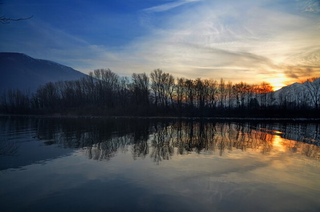 Красивый закат над озером с силуэтами деревьев, отраженных в воде