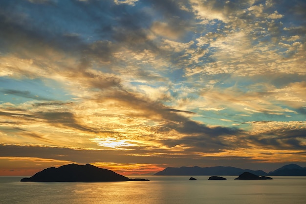 Beautiful sunset sky with clouds over the sea sunlight glare on the water Silhouettes of a range of islands on horizon Idea for background or wallpaper Breathtaking dramatic sunset vacation time