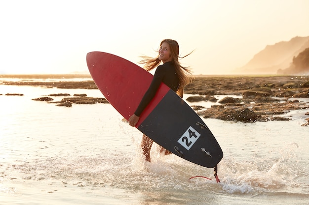 Beautiful surf girl has active lifestyle, carries surfboard, looks happily