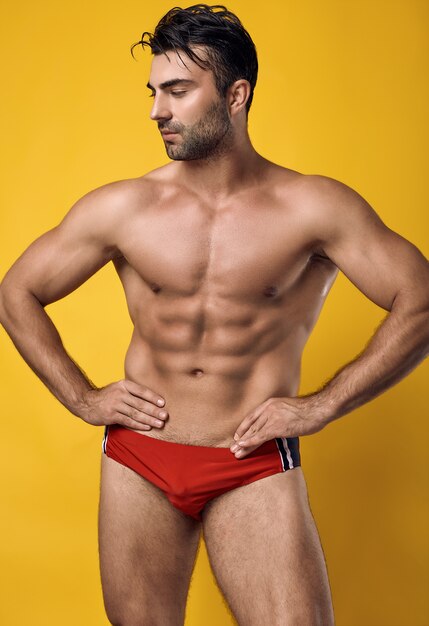Красивый загорелый мускулистый мужчина в красных купальных костюмах