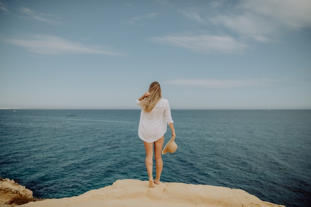 Beautiful tanned woman with raised hands looking at ocean