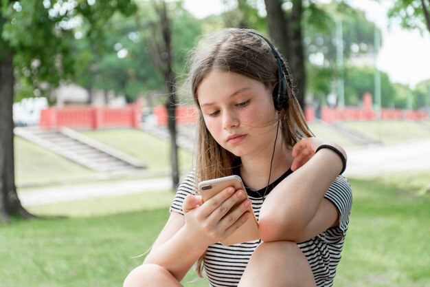 美しい十代の少女が公園で携帯電話を使用しながら音楽を聴く