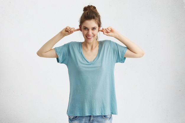 Free photo beautiful teenage girl wearing jeans and oversize blue t-shirt plugging ears with fingers and smiling broadly, teasing, pretending not to listen, ignoring someone.