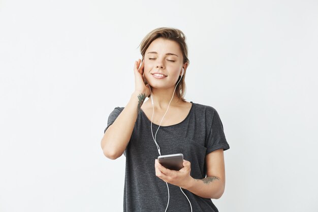 Beautiful tender young girl smiling listening music in headphones with closed eyes .