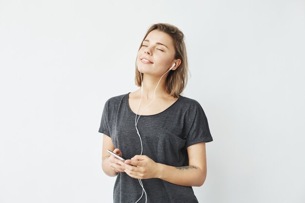 Beautiful tender young girl smiling listening music in headphones with closed eyes .