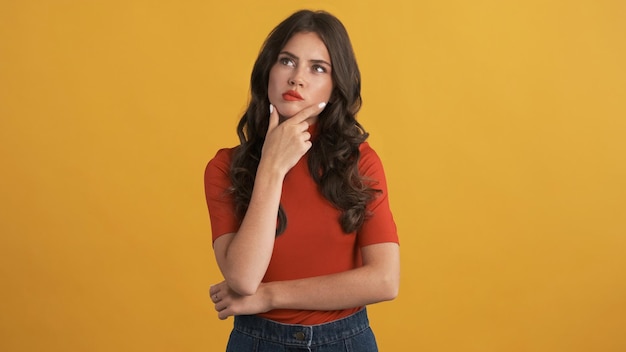 Beautiful thoughtful brunette girl in red top thinking on camera over colorful background Thinking expression