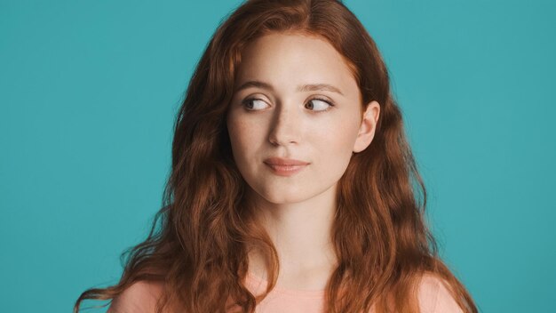 Beautiful thoughtful redhead girl slyly looking away over colorful background