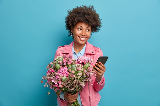 美しい思いやりのある若い女性がスマートフォンでおめでとうを受け取り、誕生日を祝う素敵な花束を手に入れる