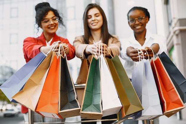 Beautiful three young women with a gift bags walk in the city. Women after shopping have fun.