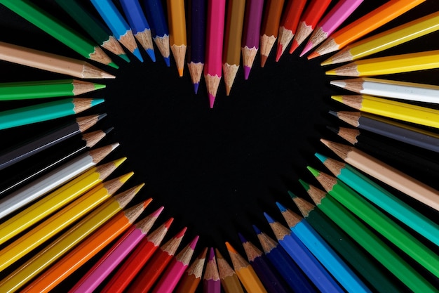 Beautiful top view of a bunch of pencils making a heart shape with a black background