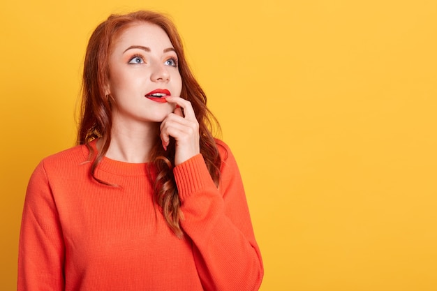 Bella ragazza alla moda in maglione arancione che è immerso nei pensieri