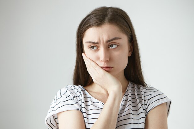 끔찍한 견딜 수없는 고통 때문에 비참하고 무기력 한 느낌, 치통으로 고통받는 동안 그녀의 뺨에 손을 찌푸리고 줄무늬 티셔츠를 입은 아름다운 불행한 학생 소녀